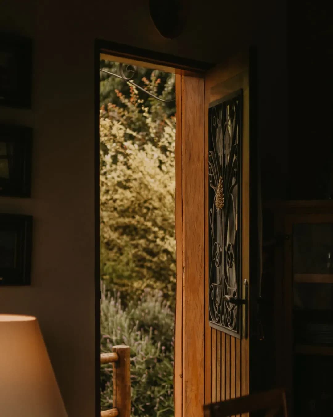 Porte en bois entrouverte sur un jardin, vue depuis une pièce éclairée par une lampe
